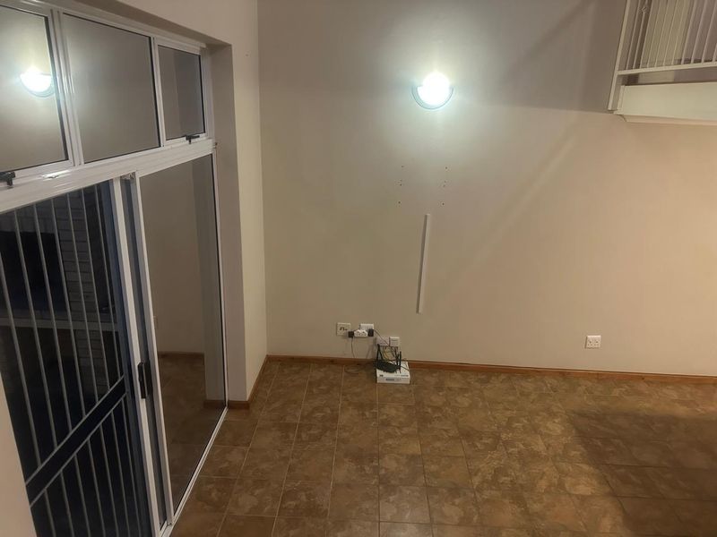 An empty living area featuring tiled flooring, a sliding glass door, and a staircase, requiring minor cosmetic updates to the walls.