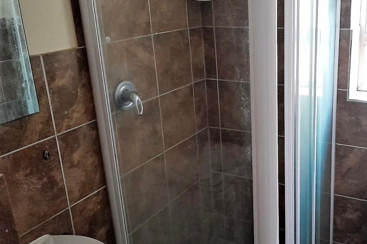 A compact bathroom featuring a shower enclosure with tiled walls and a pedestal basin.