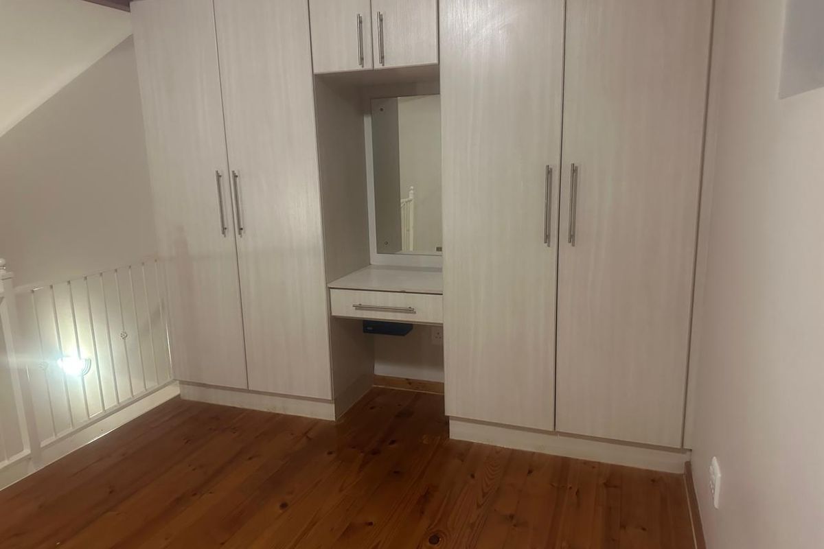 A clean bedroom featuring light-toned built-in cupboards with an integrated vanity unit and warm timber flooring.