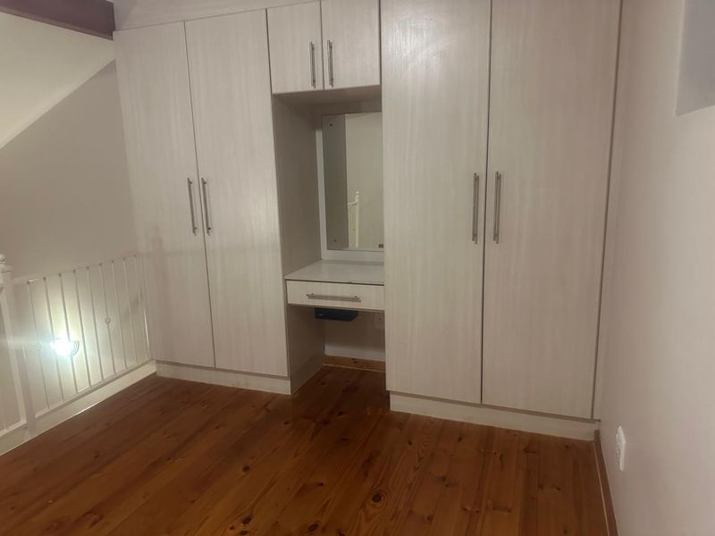 A clean bedroom featuring light-toned built-in cupboards with an integrated vanity unit and warm timber flooring.