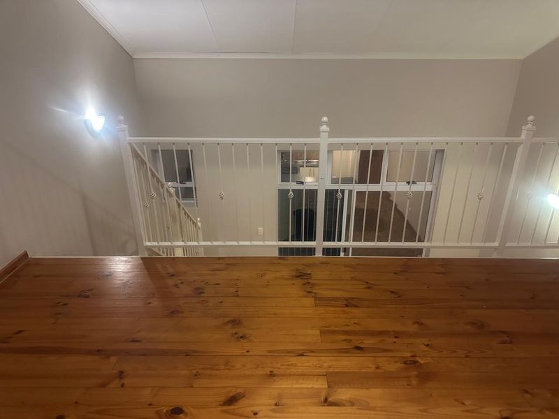 An elevated landing area featuring polished timber flooring and a white metal balustrade overlooking the lower level of the apartment.