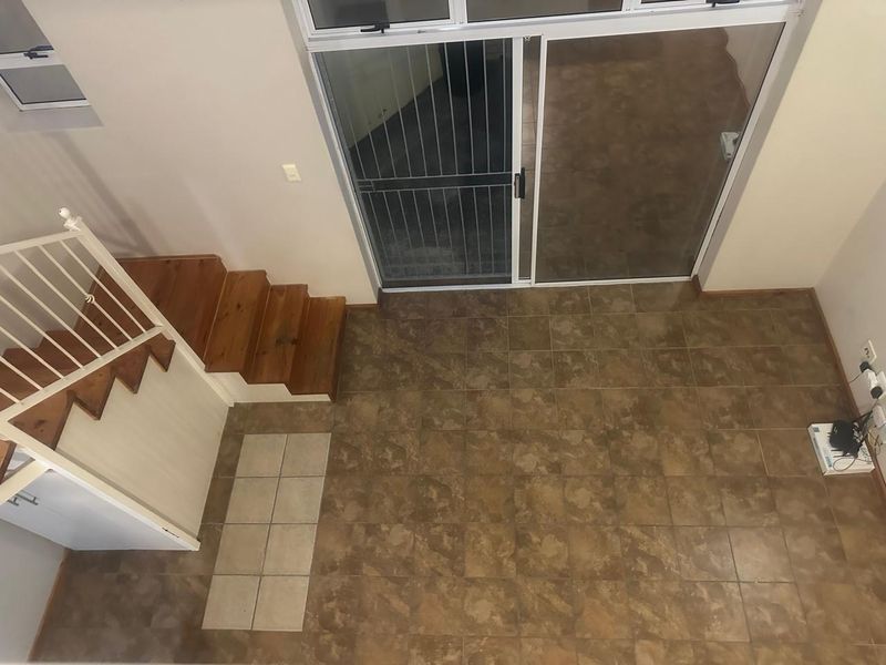 An empty living area featuring tiled flooring, a wooden staircase with a metal balustrade, and a sliding glass door leading to an outdoor space.