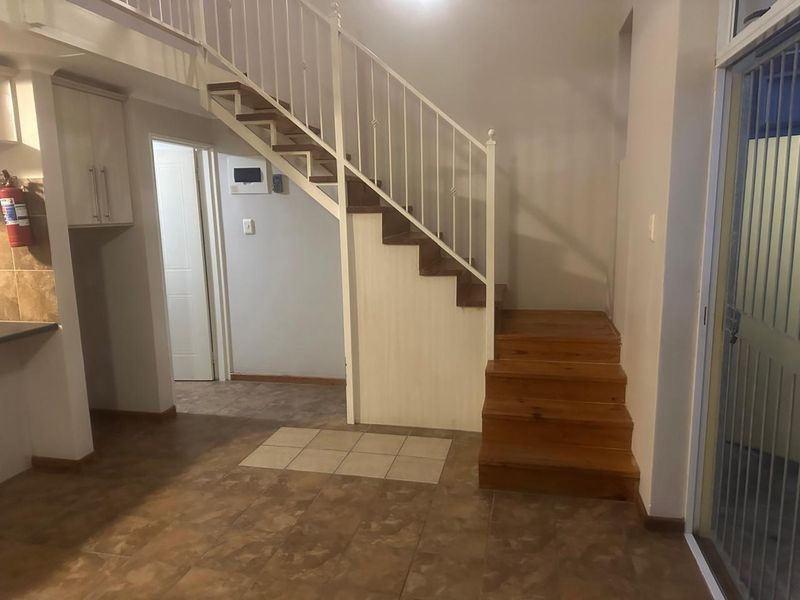 Open plan living area featuring a staircase with metal balustrade, tiled flooring, and built-in cabinetry, providing a functional layout for the apartment.