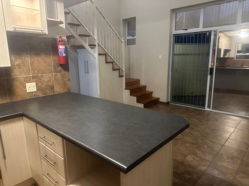 Open plan kitchen area featuring laminate countertops, tiled backsplash, and a staircase leading to the upper level, with direct access to an outdoor space.