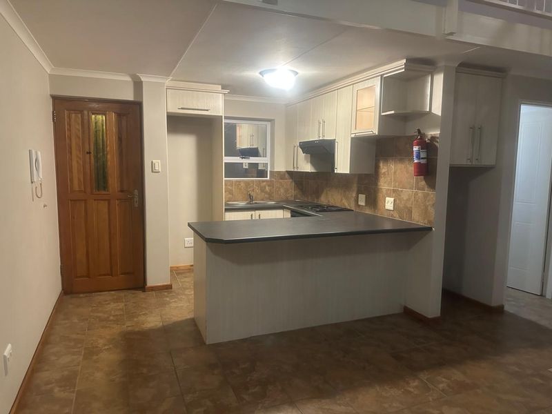 Functional kitchen featuring built-in cabinetry, laminate countertops, a hob with extractor fan, and tiled backsplash, offering a practical layout for daily use.