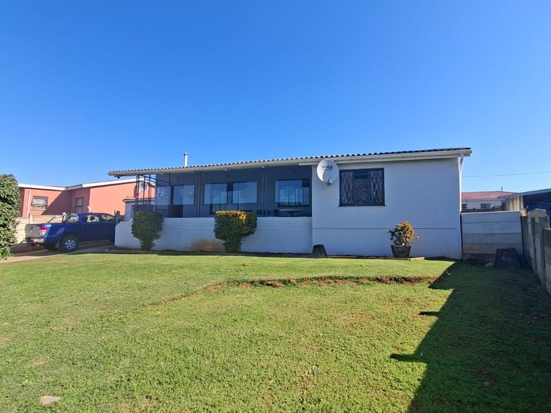Rear view of the property featuring a spacious lawn, enclosed patio area, and concrete boundary walling.