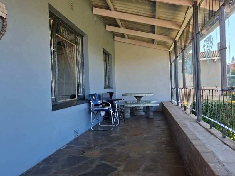 A covered patio area featuring stone flooring, exposed rafters, and metal security screening, providing a functional outdoor space.