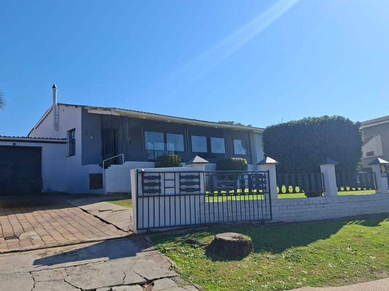 Front view of a single-story house featuring a paved driveway, single garage, enclosed patio, and a perimeter wall with a metal gate.