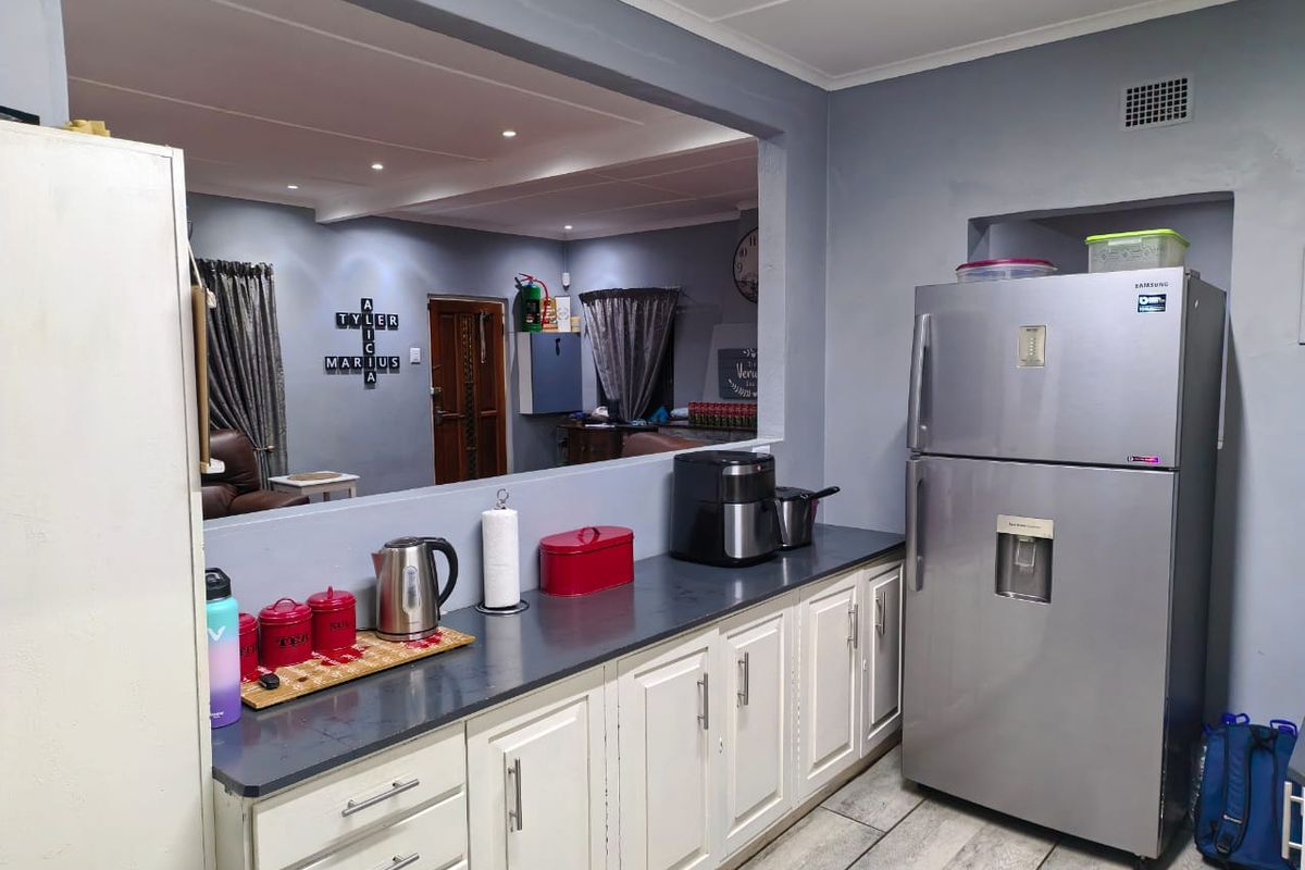 A functional kitchen featuring white cabinetry, dark countertops, and tiled flooring, with a large serving hatch opening into the adjacent living area.