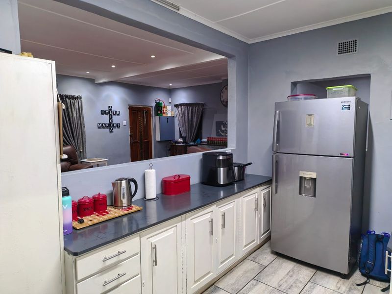 A functional kitchen featuring white cabinetry, dark countertops, and tiled flooring, with a large serving hatch opening into the adjacent living area.