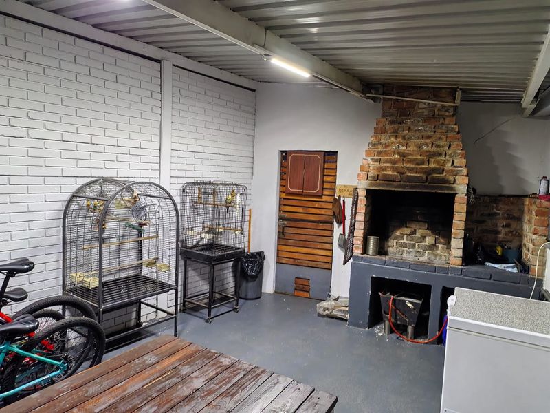 Covered outdoor patio area featuring a built-in brick braai, painted brick walls, and a corrugated metal ceiling.