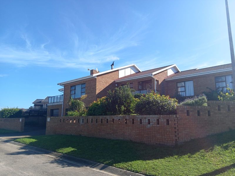 A street-facing view of a double-storey brick house featuring a tiled roof, balcony, and a low brick boundary wall.