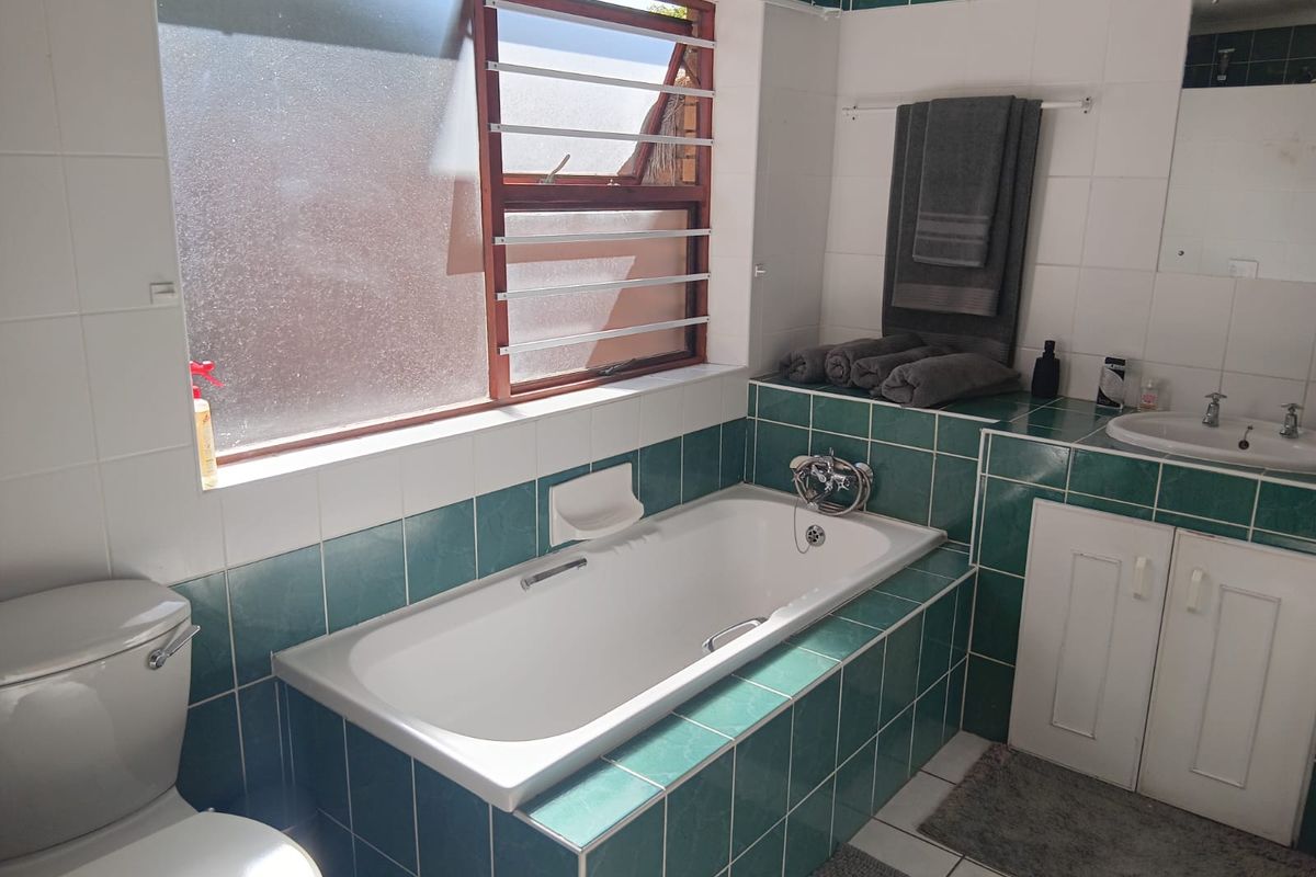 A functional bathroom featuring a built-in bathtub, vanity cabinet with basin, and toilet, finished with green and white wall tiling.