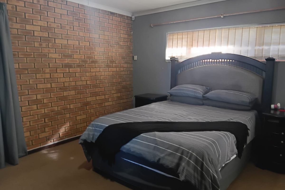 A bedroom featuring an exposed brick feature wall, neutral painted walls, and vertical window blinds.