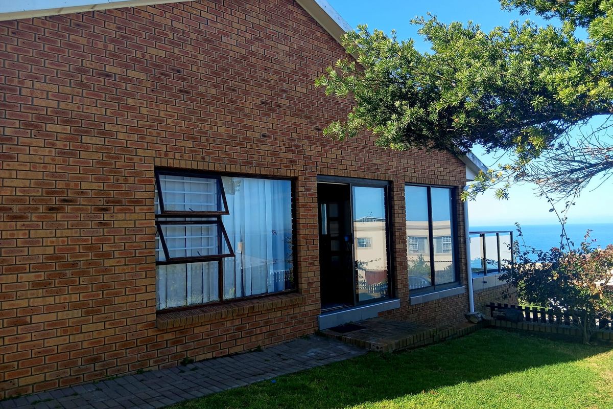 Rear view of a face brick house featuring large windows, a sliding door, and a glass balustrade overlooking the ocean.