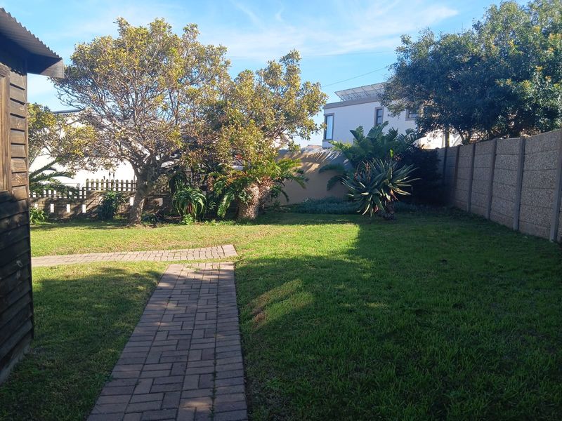 A private rear garden featuring a paved walkway, established trees, and secure boundary walling.