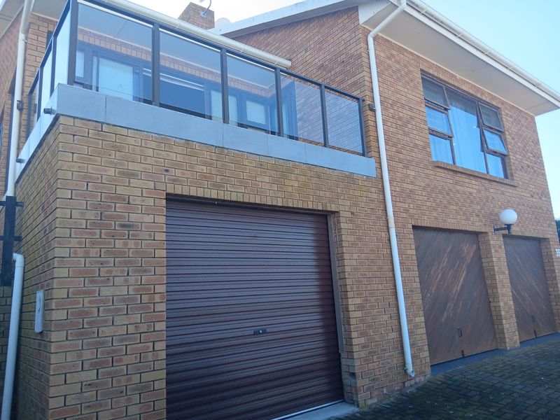 Front elevation of a double-storey brick house featuring a balcony with glass balustrade and multiple garage doors.