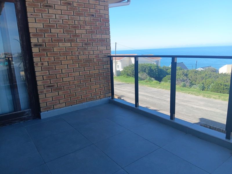A clean, tiled balcony featuring a modern metal and glass balustrade, offering clear views of the surrounding landscape and ocean.