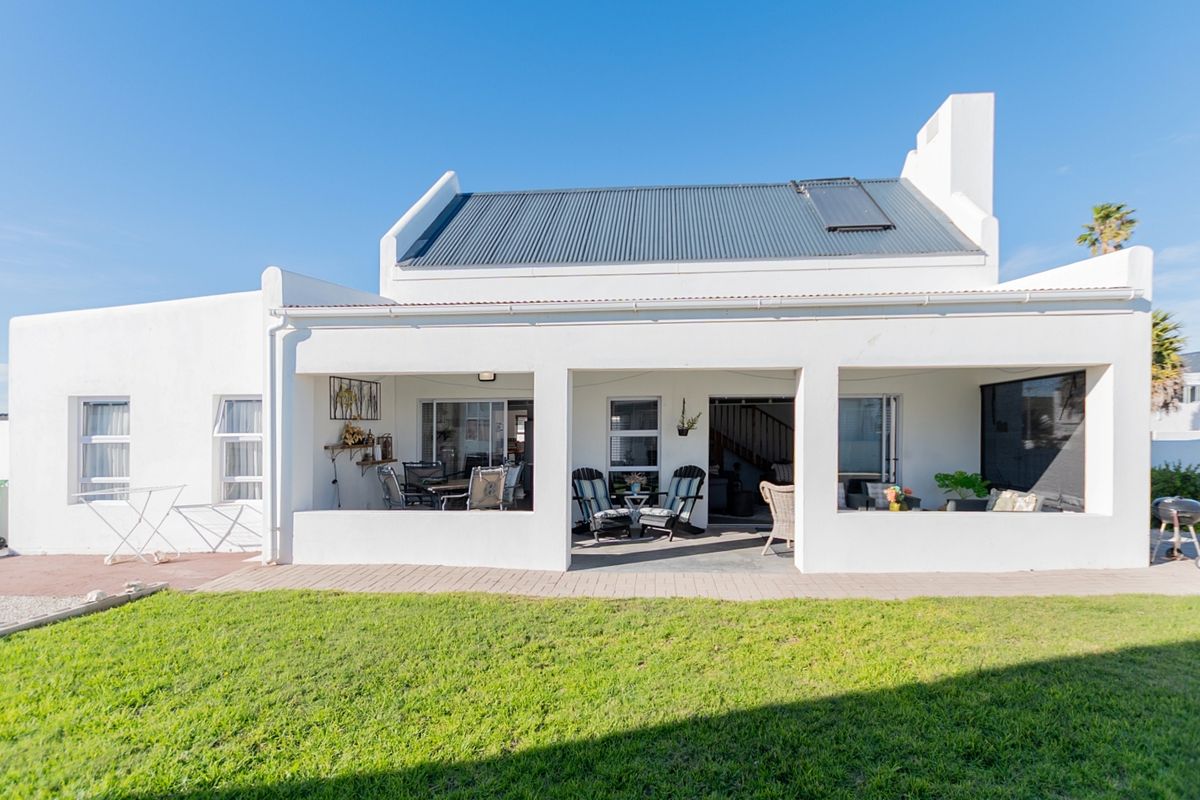 Rear view of the house featuring a covered patio area, corrugated metal roof with solar heating, and a well-maintained lawn.