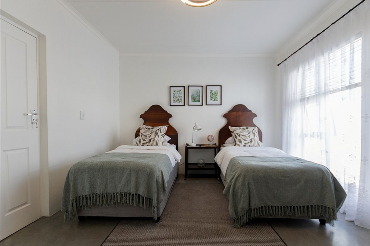 A well-maintained bedroom featuring polished concrete flooring, neutral white walls, and natural light through a large window with sheer curtains.