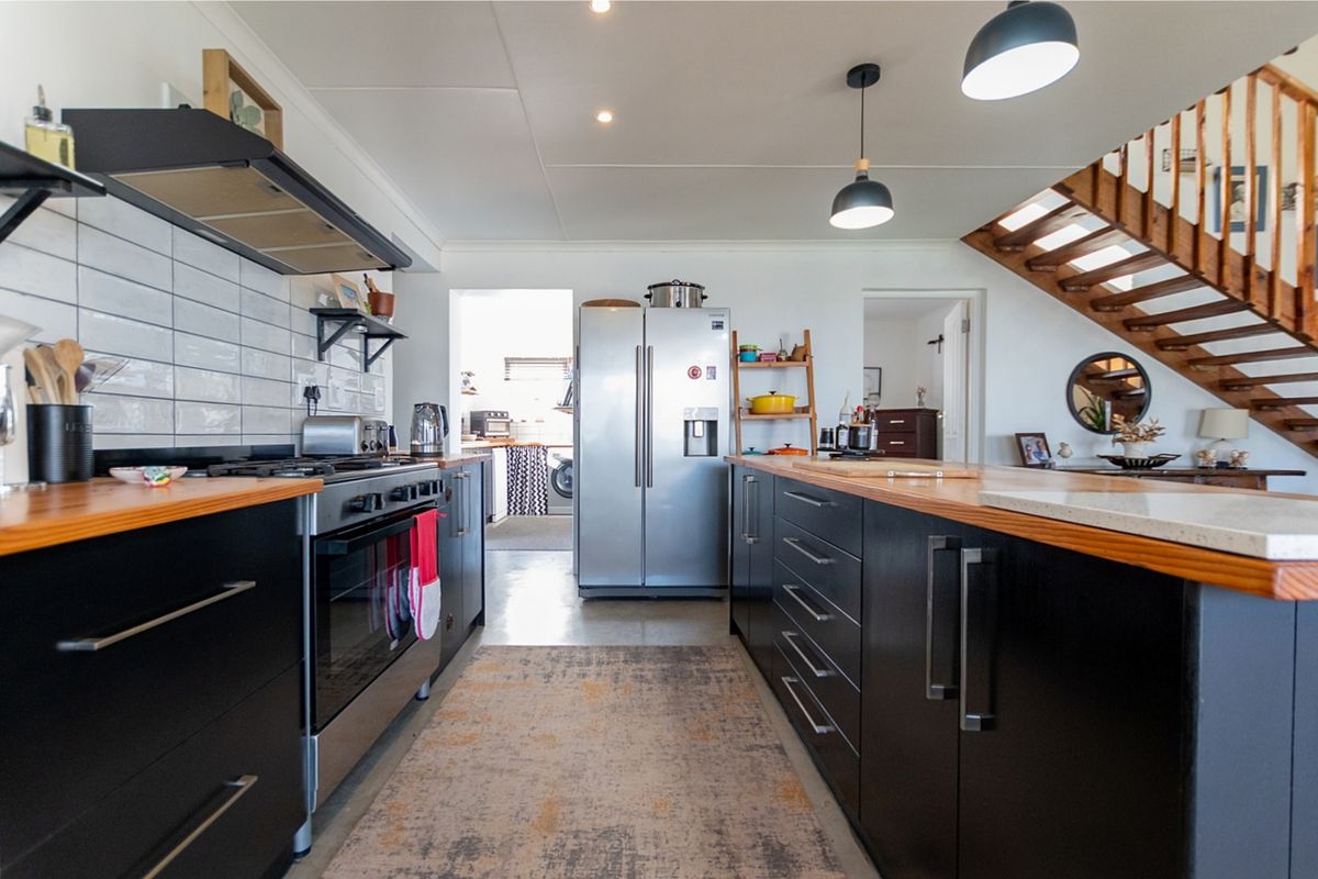 Modern kitchen featuring dark cabinetry, timber countertops, subway tile backsplash, and a gas stove, with an open-plan layout leading to a staircase.