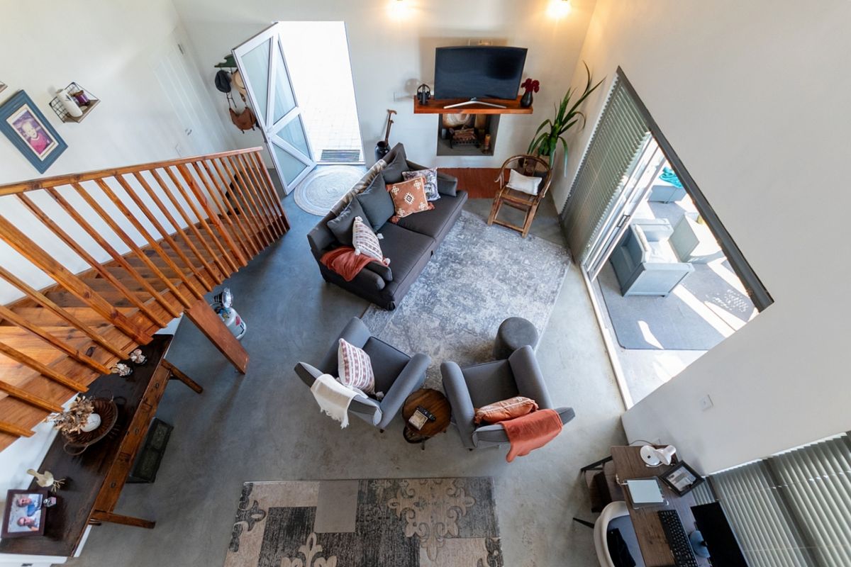 An open-plan living area featuring polished concrete floors, a wooden staircase, a fireplace with a mantel, and sliding glass doors leading to the patio.