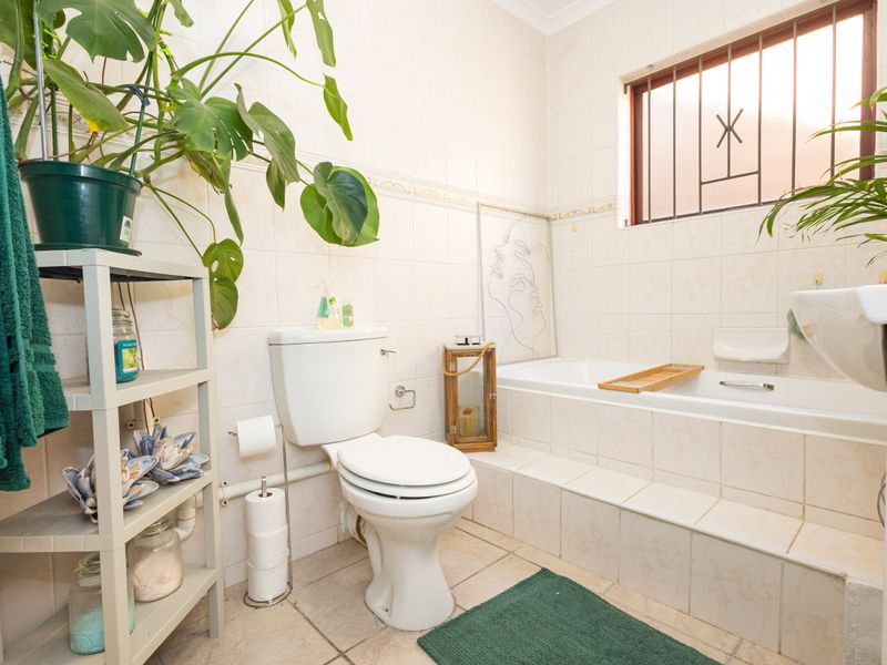 A functional bathroom featuring a built-in bathtub, pedestal basin, and toilet, finished with neutral ceramic wall and floor tiles.