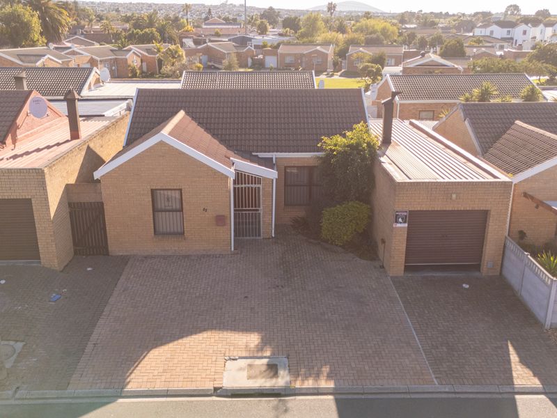 Aerial view of a single-story brick house featuring a tiled roof, paved driveway, and integrated garage in a residential neighborhood.