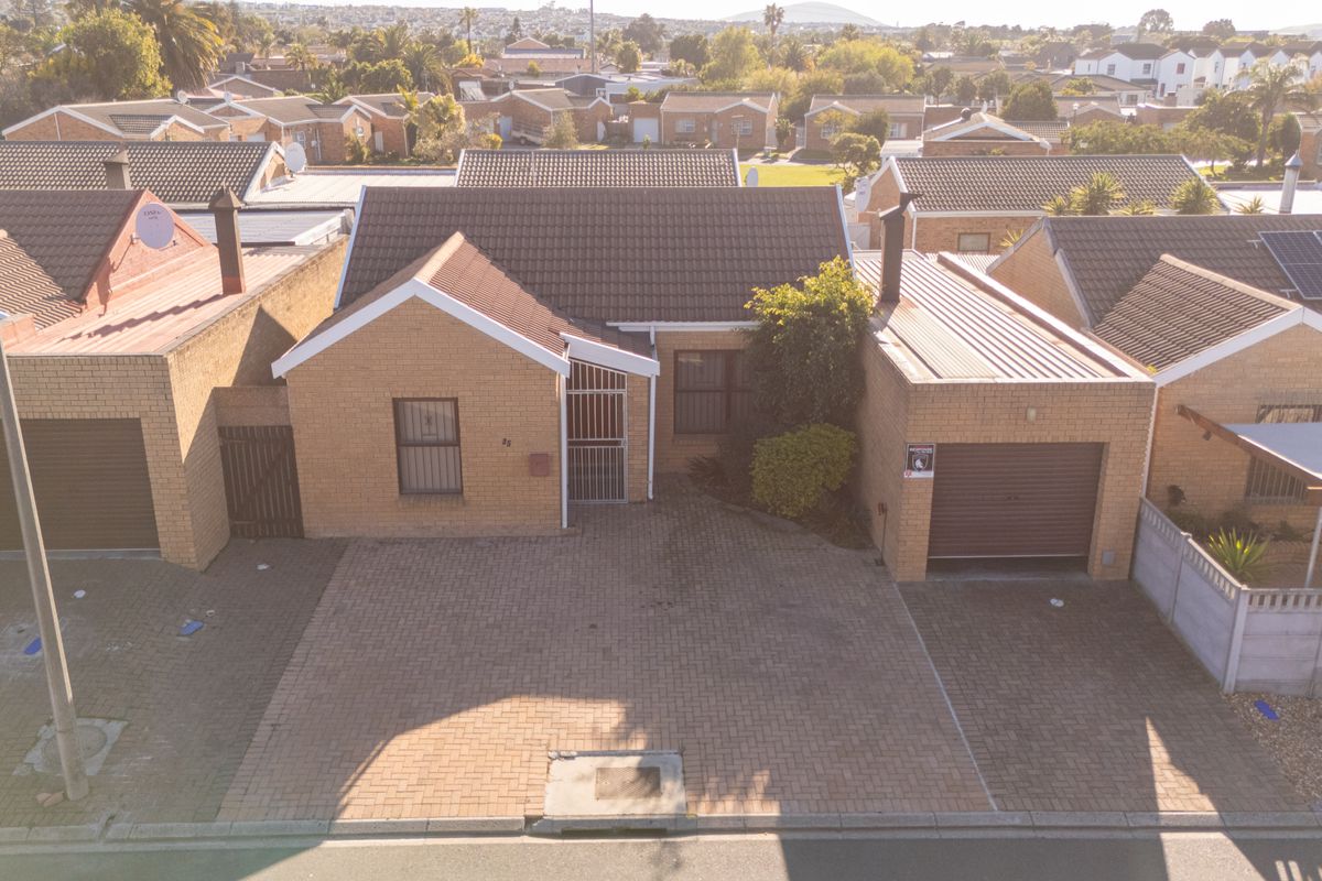 Aerial view of a single-story brick house featuring a tiled roof, paved driveway, and integrated garage in a residential neighborhood.