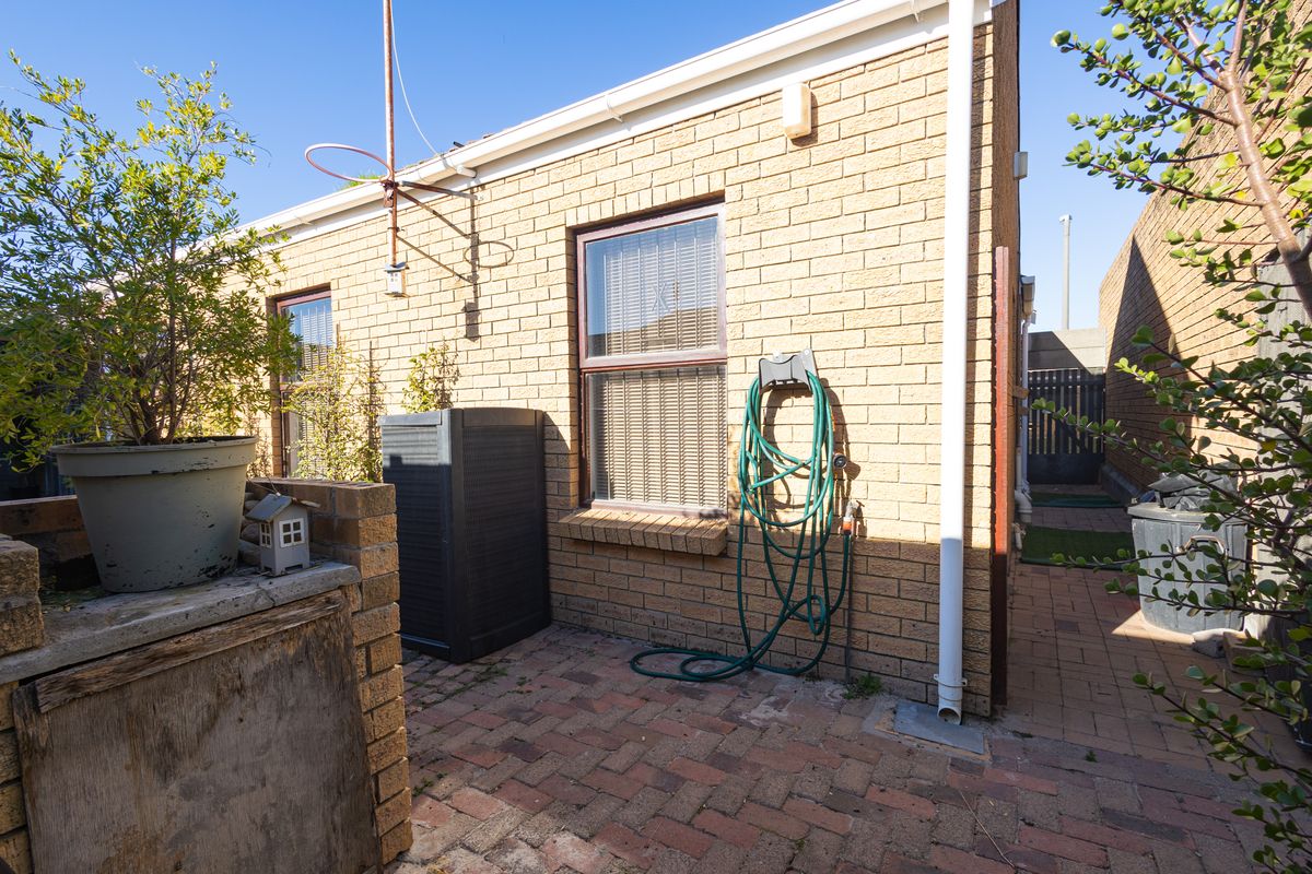 A rear exterior view of the property featuring a brick facade, paved patio area, and functional drainage downpipes.