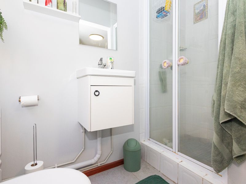 Compact bathroom featuring a wall-mounted vanity, shower enclosure with glass doors, and tiled finishes. Requires minor cosmetic updates to improve overall presentation.