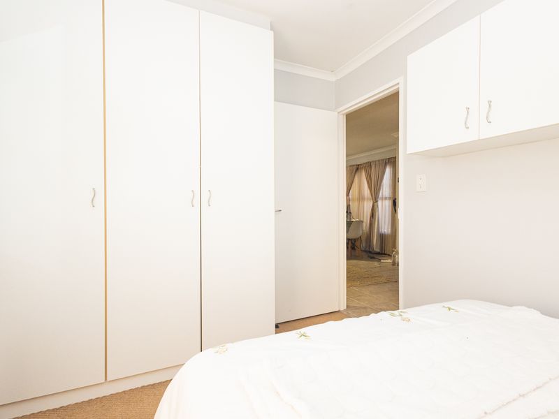 A clean bedroom featuring ample built-in cupboard space and overhead storage cabinets, finished with neutral carpeting and classic cove cornicing.