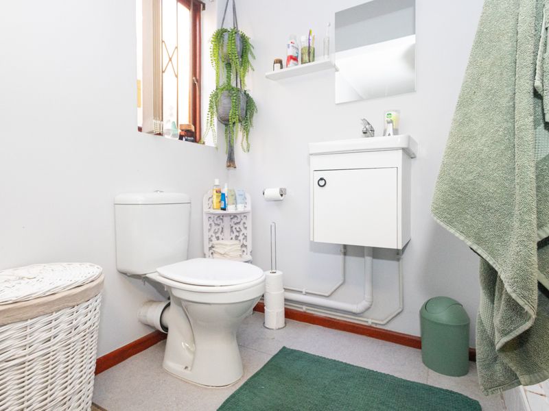 A functional bathroom featuring a wall-mounted vanity, basin, and toilet, with tiled flooring and a window providing natural light.