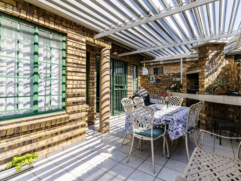 Covered patio area featuring a built-in braai, brick wall finishes, and a louvred roof, providing a functional outdoor entertainment space.
