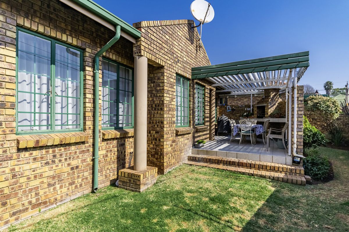 Rear exterior view of the townhouse featuring a brick facade, a covered patio with a built-in braai, and a small private garden area.