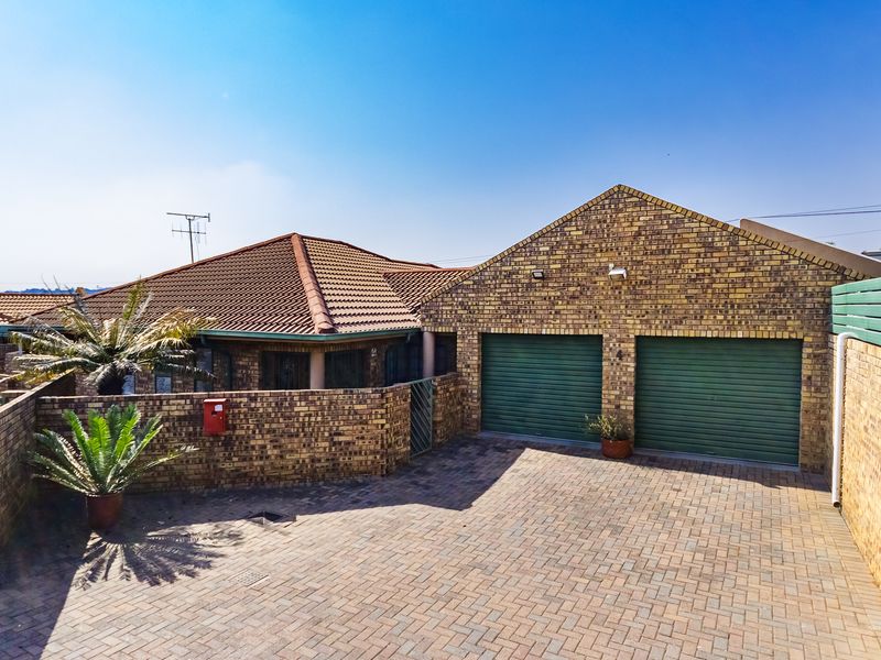 Front view of a townhouse featuring a face brick facade, a paved driveway, and a double garage with green roll-up doors.