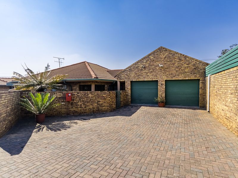Front exterior view of a townhouse featuring a double garage with roller shutter doors, facebrick construction, and paved driveway.