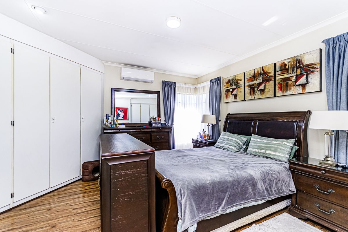 A well-maintained bedroom featuring laminate flooring, built-in cupboards, and a wall-mounted split-system air conditioning unit.
