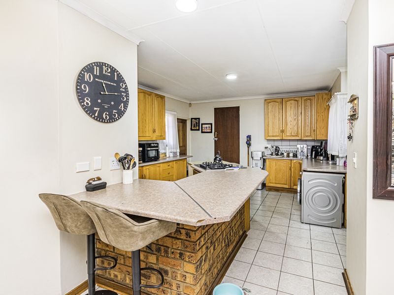 A functional kitchen featuring wooden cabinetry, a brick-base breakfast bar, gas hob, and tiled flooring, offering a practical layout for daily meal preparation.