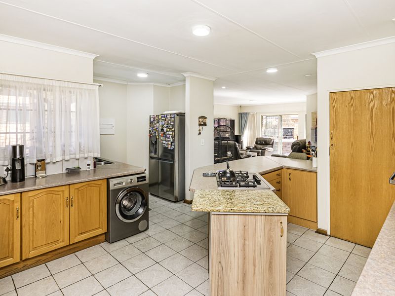 Open-plan kitchen featuring wooden cabinetry, gas hob, and tiled flooring, flowing into the adjacent living area.