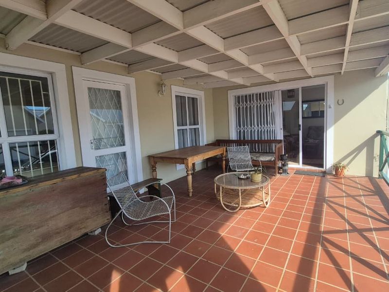 A spacious covered patio featuring terracotta floor tiles, exposed beam ceiling, and direct access to the interior through sliding glass doors.