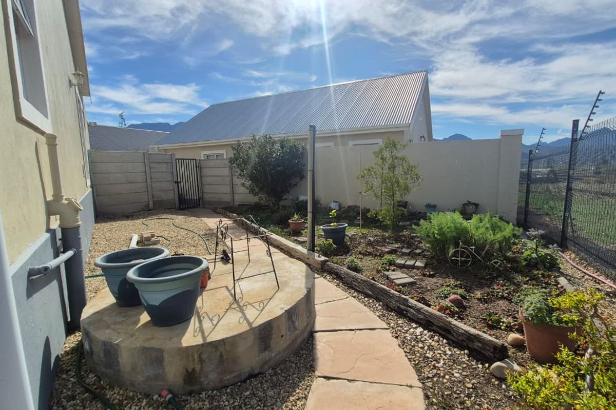 A rear garden area featuring a paved walkway, raised concrete platform, and secure boundary walling with electric fencing.