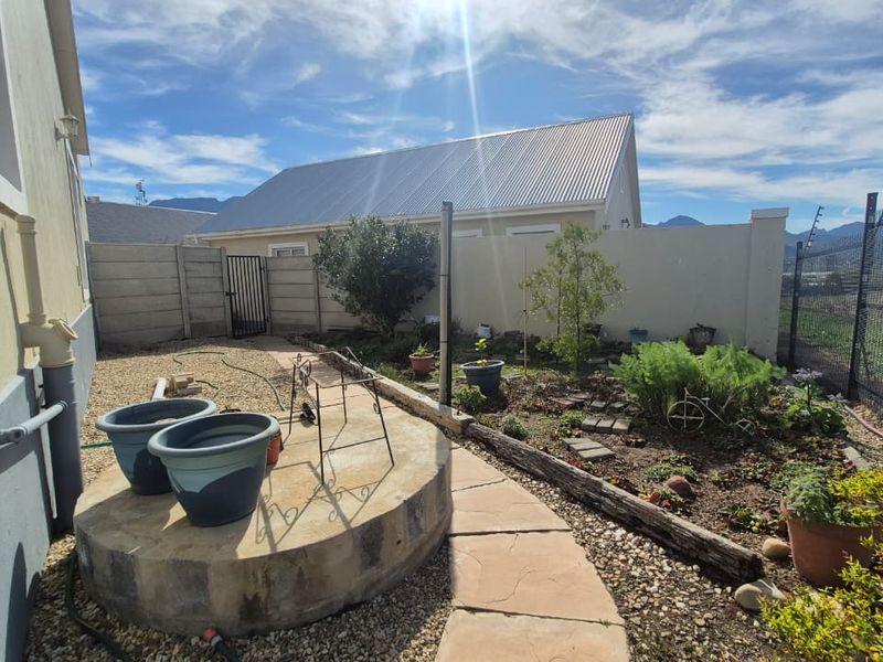 A rear garden area featuring a paved walkway, raised concrete platform, and secure boundary walling with electric fencing.