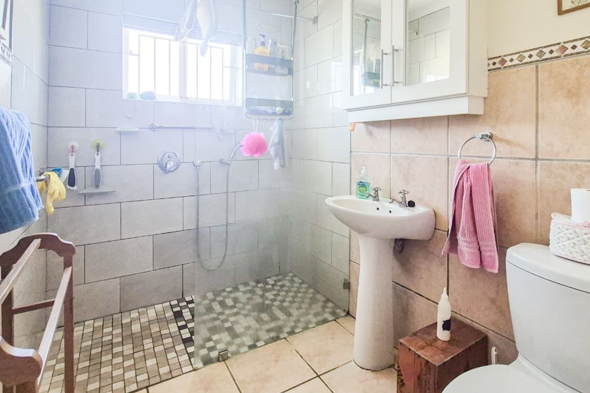 A functional bathroom featuring a walk-in shower with glass screen, pedestal basin, and tiled finishes throughout.