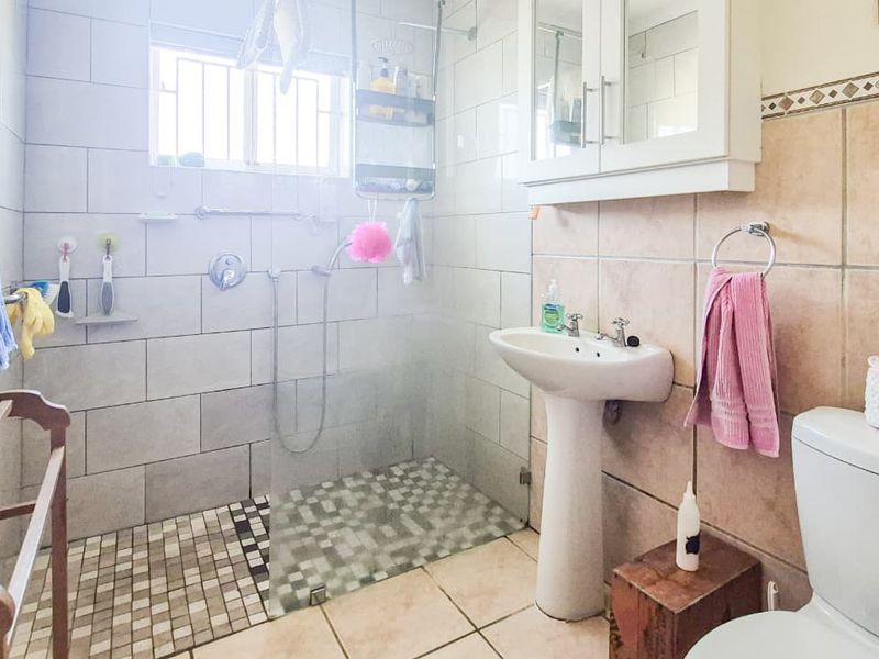 A functional bathroom featuring a walk-in shower with glass screen, pedestal basin, and tiled finishes throughout.