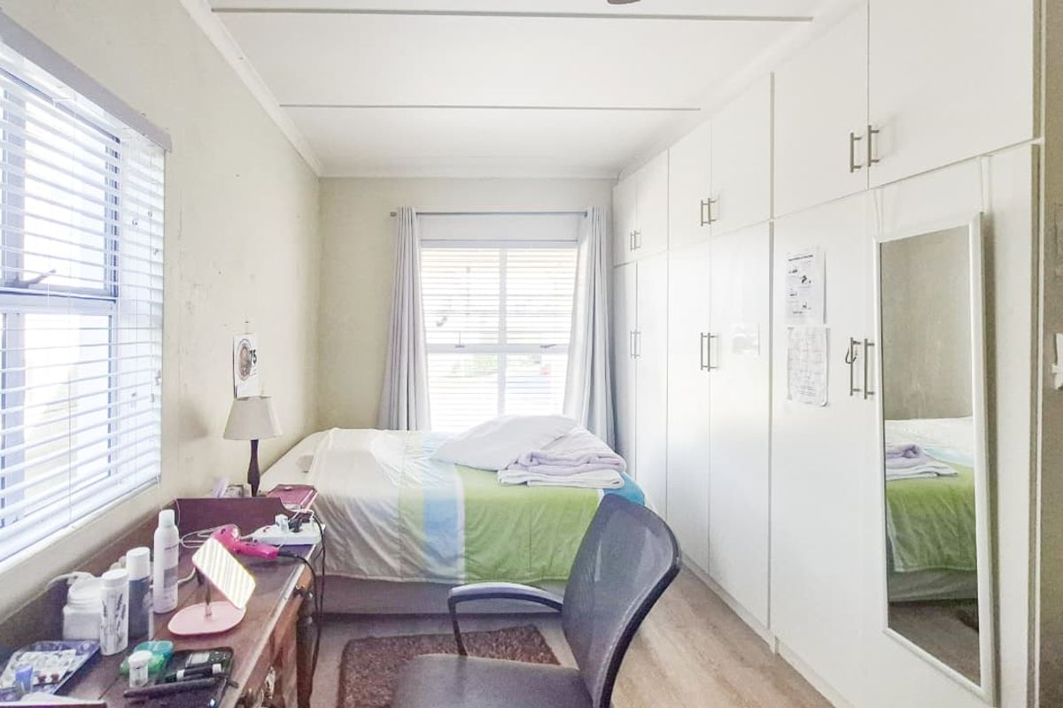 A functional bedroom featuring extensive built-in storage cupboards, laminate flooring, and dual windows with venetian blinds for natural light.
