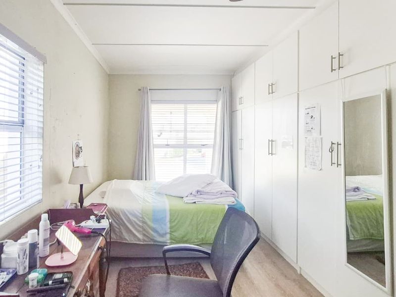 A functional bedroom featuring extensive built-in storage cupboards, laminate flooring, and dual windows with venetian blinds for natural light.