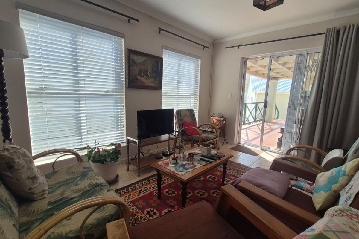 A comfortable living room featuring tiled flooring, large windows with venetian blinds, and a sliding glass door providing access to an outdoor patio area.