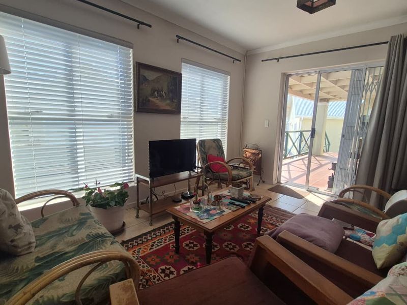 A comfortable living room featuring tiled flooring, large windows with venetian blinds, and a sliding glass door providing access to an outdoor patio area.