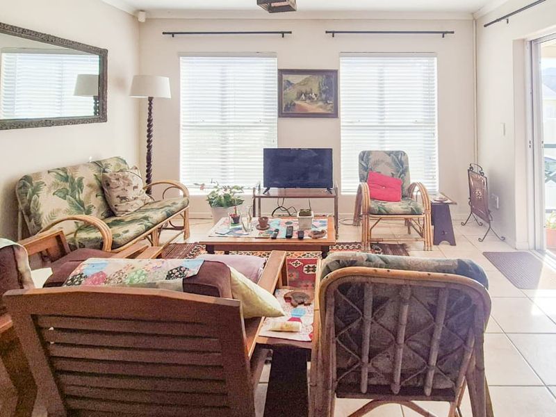 A bright living room featuring tiled flooring, large windows with venetian blinds, and a sliding glass door providing access to the outdoor area.